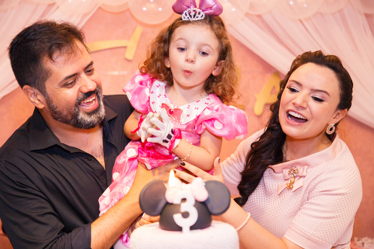 Família reunida atrás do bolo na hora do parabéns, com a criança soprando a velinha.