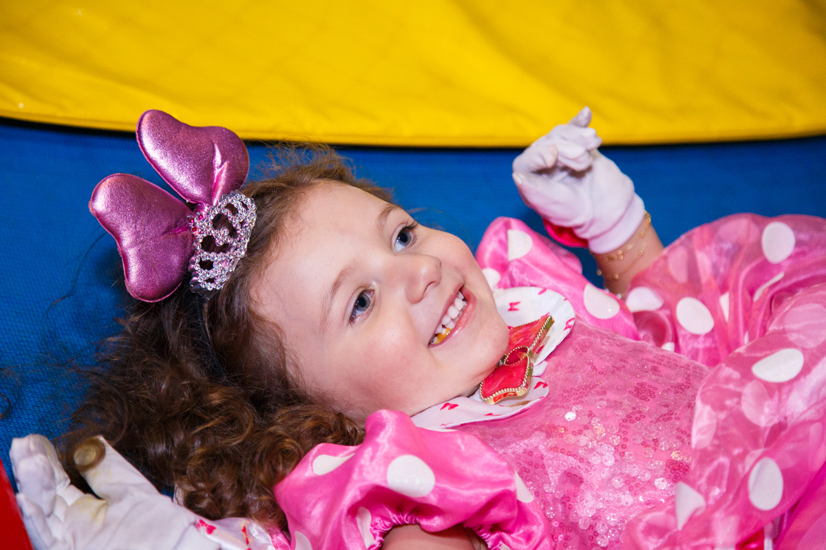 Criança em seu aniversário infantil, deitada no pula pula após desequilibrar e cair, dando um sorriso.