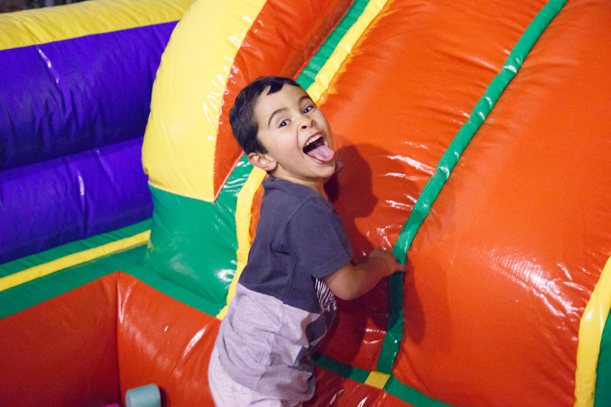 Criança dentro da piscina de bolinhas do brinquedão inflável fazendo uma careta para a foto, com a língua de fora.