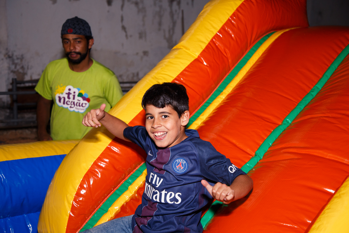 Criança escorrgando no brinquedão inflável, sorrindo e fazendo joia para as fotos.