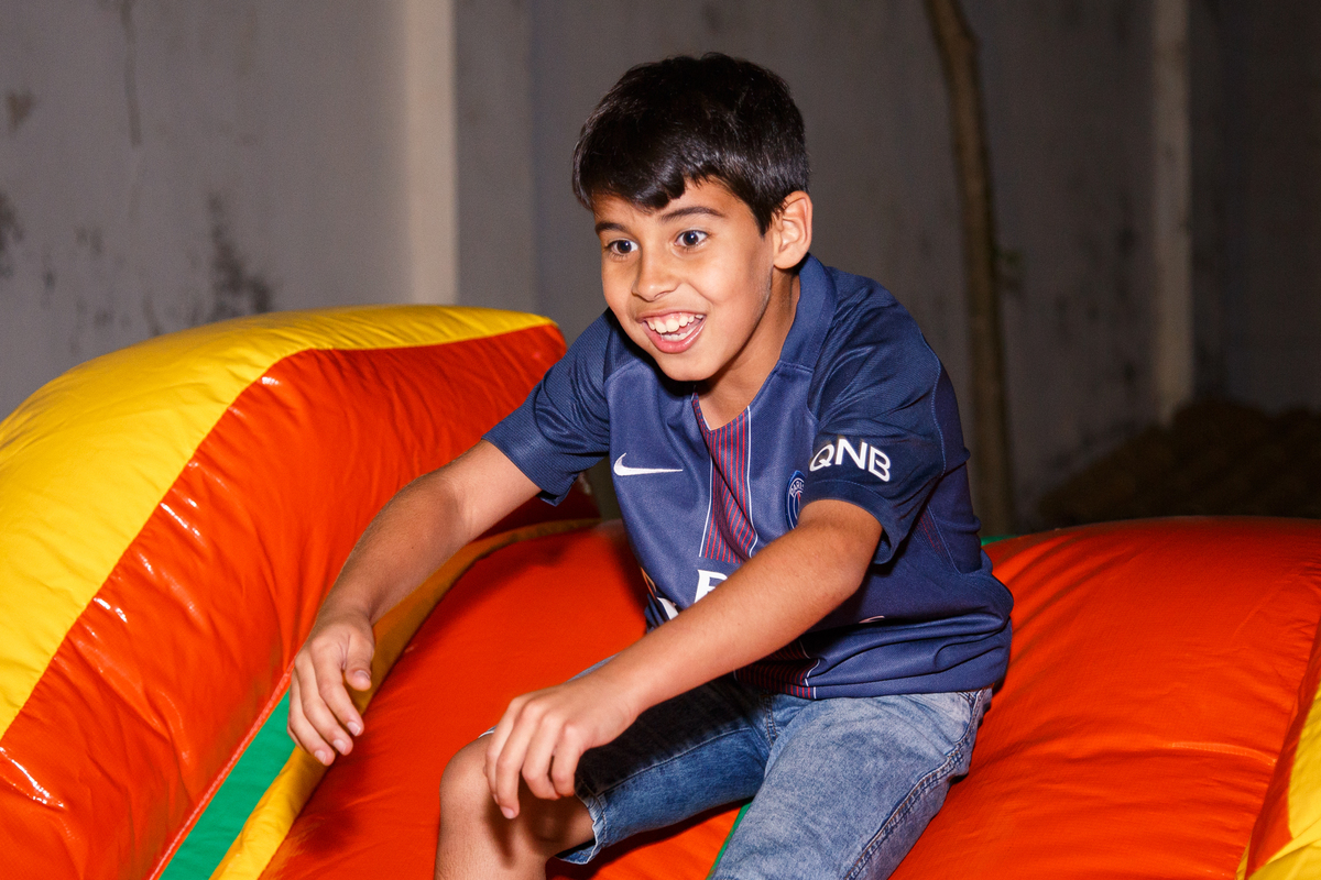 Criança sorrindo e brincando de escorregar no brinquedão inflável.