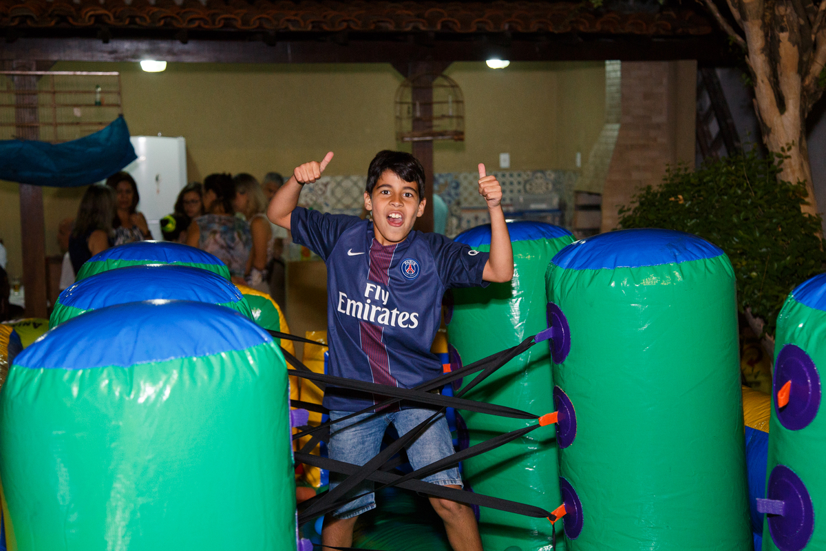 Criança em seu aniversário infantil brincando no brinquedão inflável, posando para foto fazendo sinal de joia com as duas mãos.
