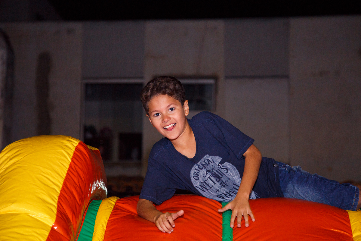 Criança posando para foto e sorrindo ao acabar de subir a rampa para escorregar para a piscina de bolinhas no brinquedão inflável.