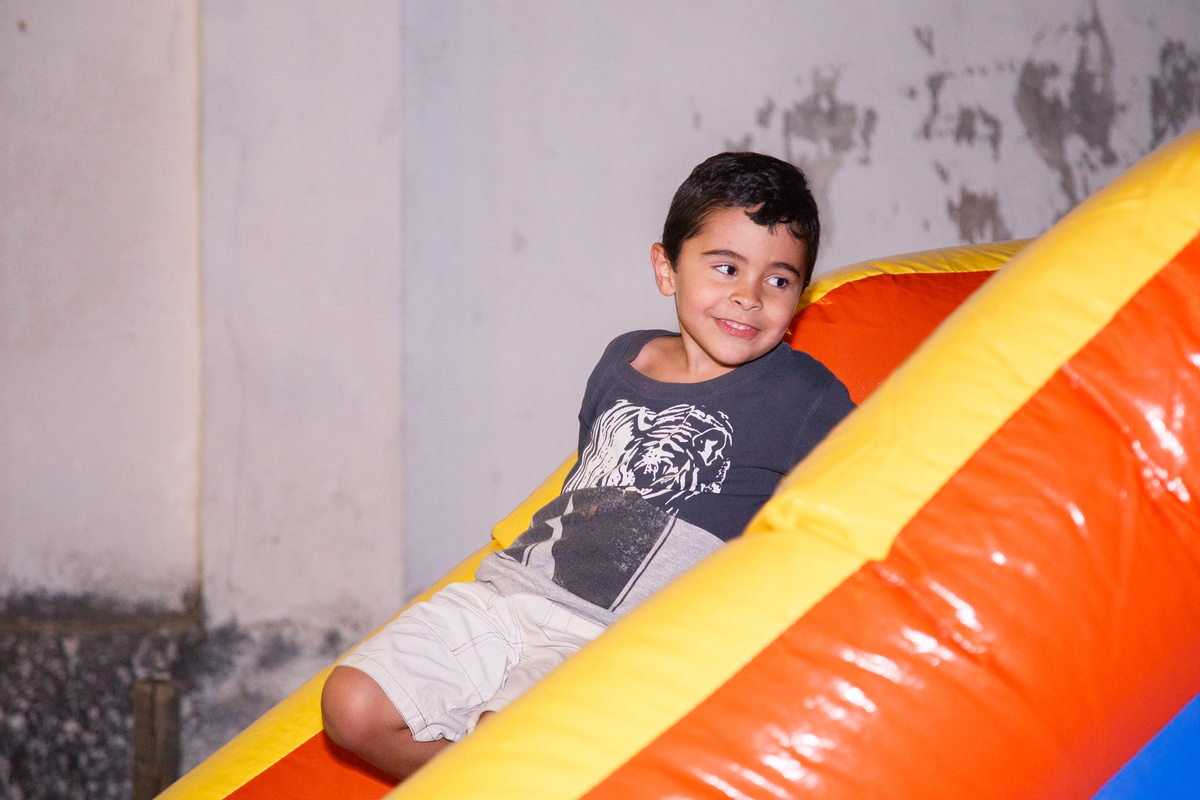 Criança brincando de escorregar no brinquedão inflável, olhando para o lado e dando um meio sorriso.