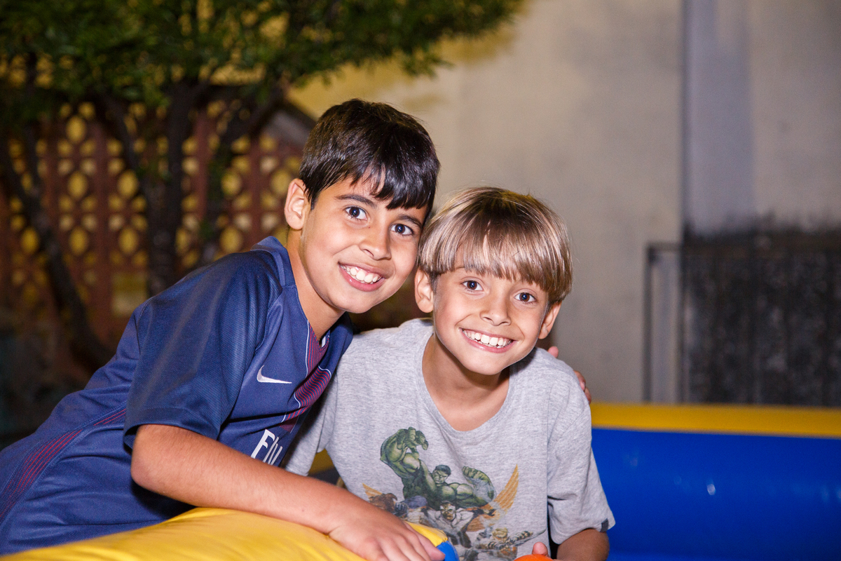 Criança em seu aniversário de 9 anos posando dentro do brinquedão inflável com um de seus amigos, ambos sorrindo e olhando para a câmera.