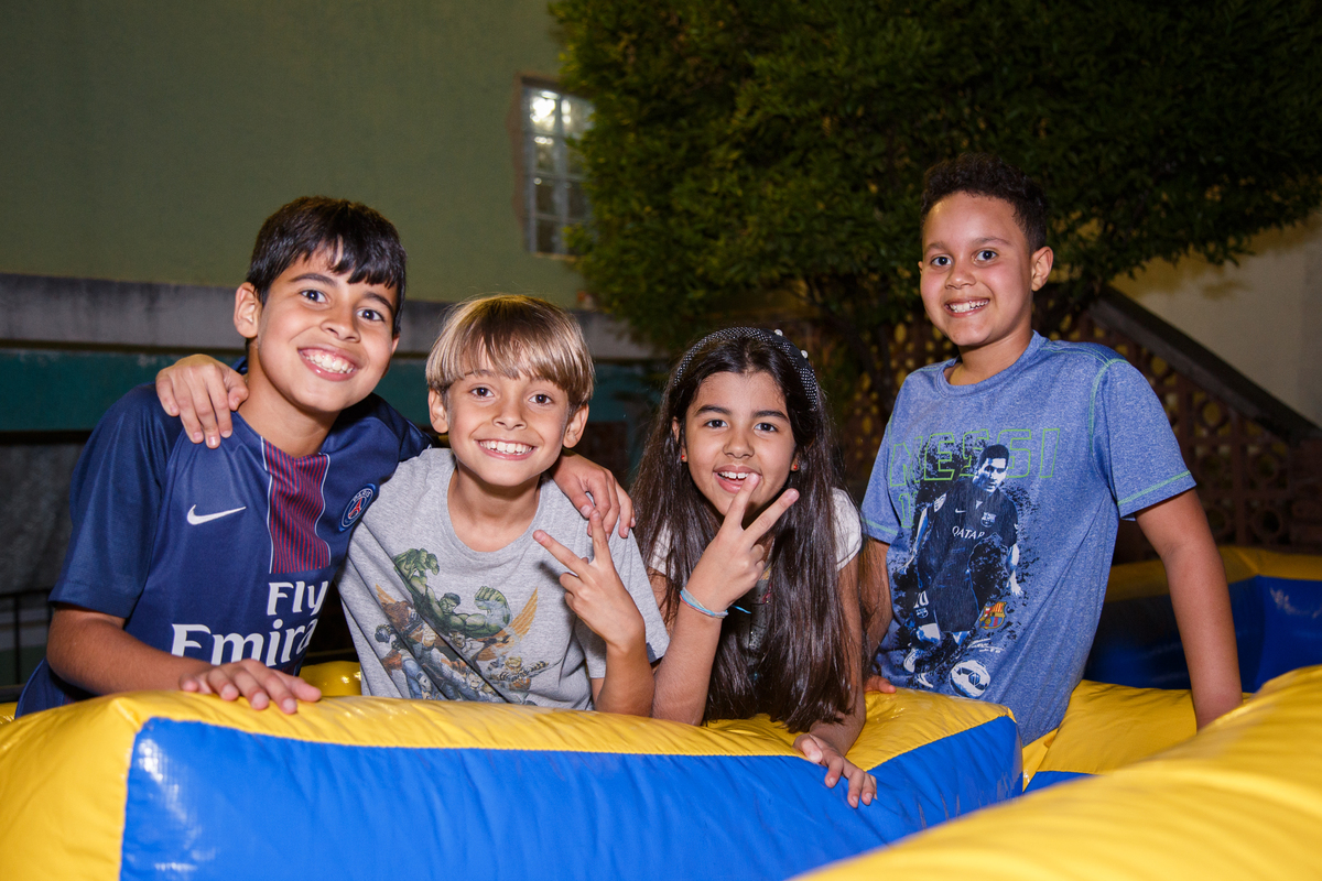 Quatro crianças em um aniversário infantil, dentro de um brinquedão inflável posando para a foto, sorrindo.