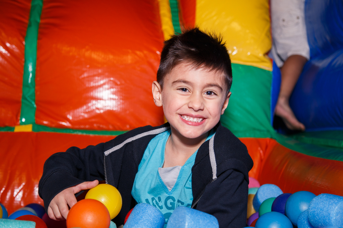 Criança dentro da piscina de bolinhas do brinquedão inflável, sentada e sorrindo para a foto.
