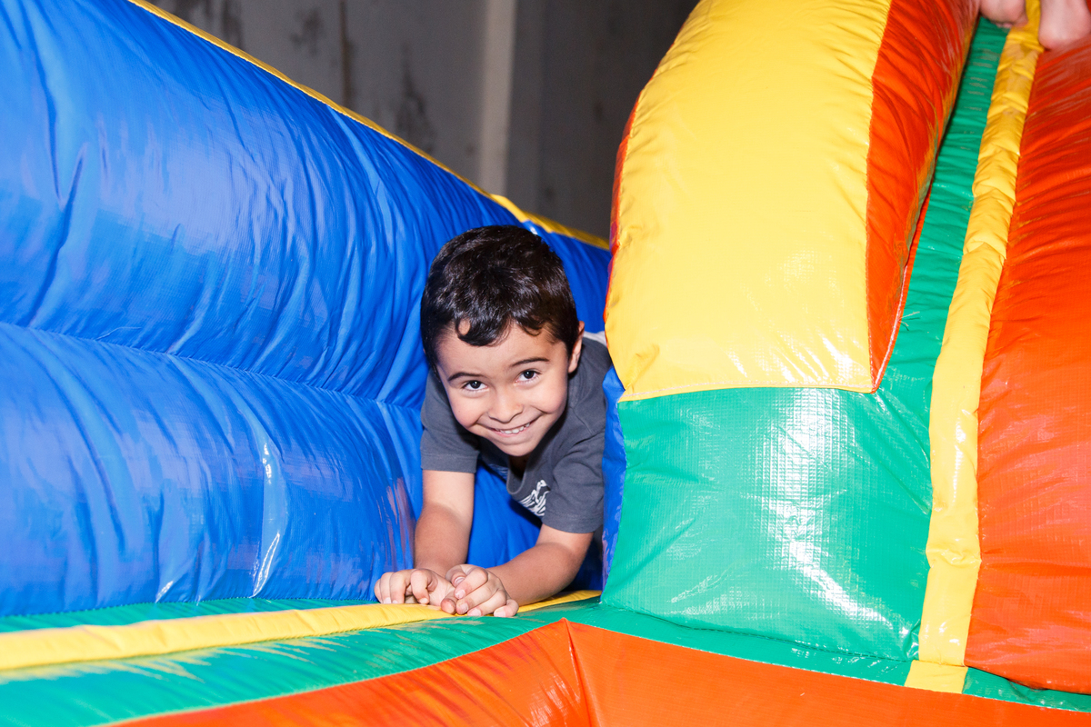 Criança brincando dentro do brinquedão inflável, passando entre a borda do brinquedo e a rampa de escorrega com um sorriso sapeca.
