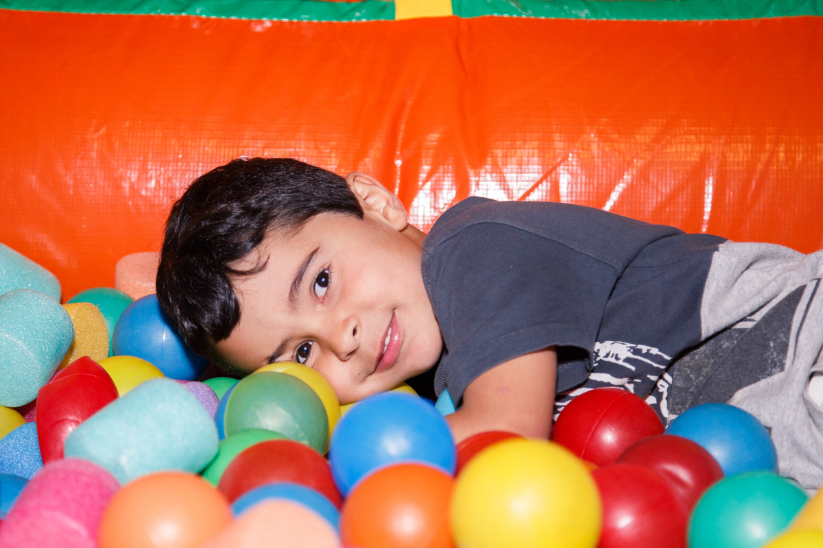 Criança deitada dentro da piscina de bolinhas do brinquedão inflável no aniversário infantil do seu irmão, com carinha de cansado.