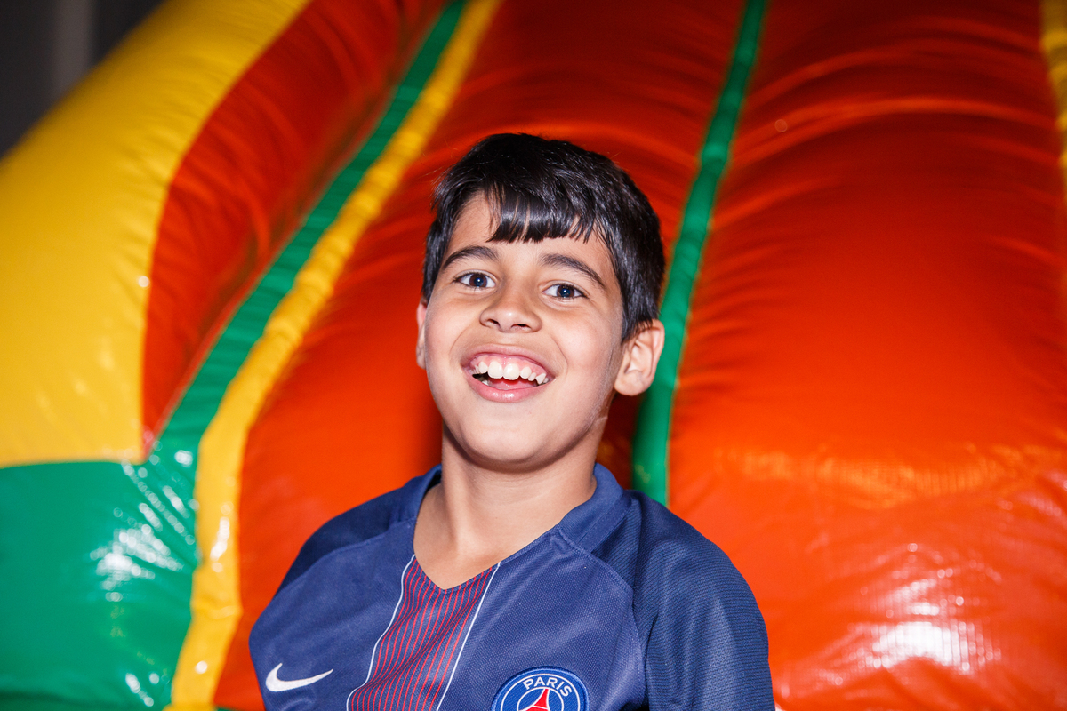 Criança em seu aniversário de 9 anos após escorregar para dentro da piscina de bolinhas, com um sorriso, olhando para a câmera.