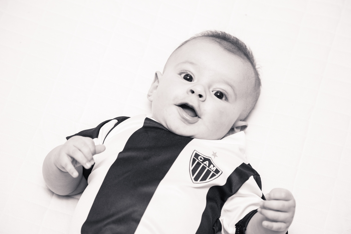 Foto em preto e branco de um bebê deitado de barriga para cima com uma camisa do Atlético, Galo, e olhando para a câmera.