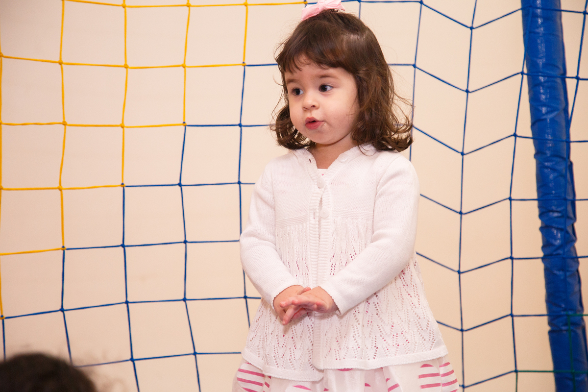 Menina de 2 anos no pula pula de sua festa de aniversário, usando um vestido branco com detalhes rosa e um casaquinho branco.