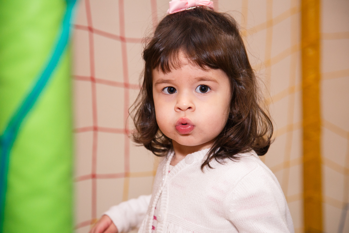 Menina de 2 anos no pula pula de sua festa de aniversário, usando um vestido branco com detalhes rosa e um casaquinho branco.