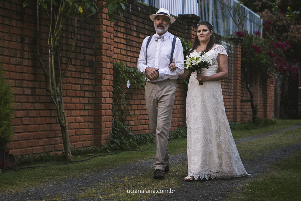 noiva com seu lindo vestido rendado entra com pai em cerimônia ecumenica