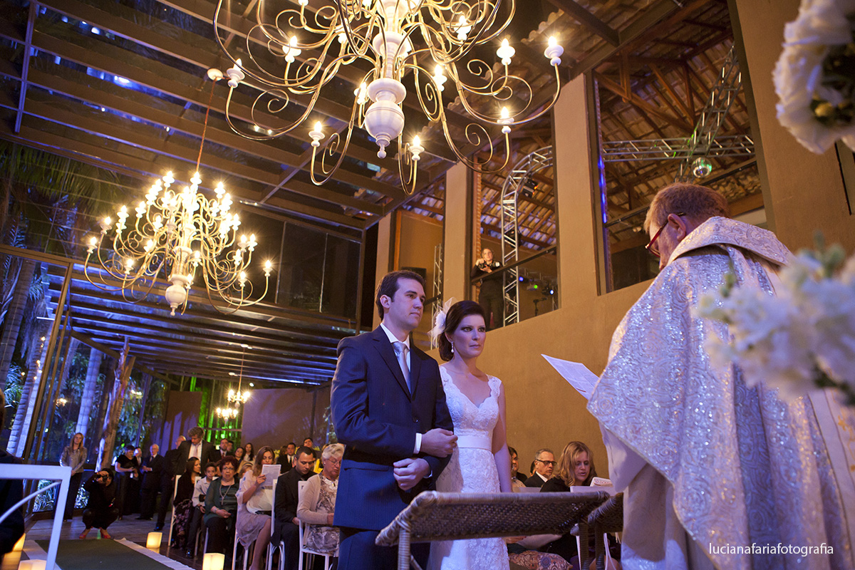 noivos no altar com o padre de caldas celebrante para casamento no salão casamento a noite no la farme no salão de vidro salão rustico com lustres gigantes e maravilhosos
