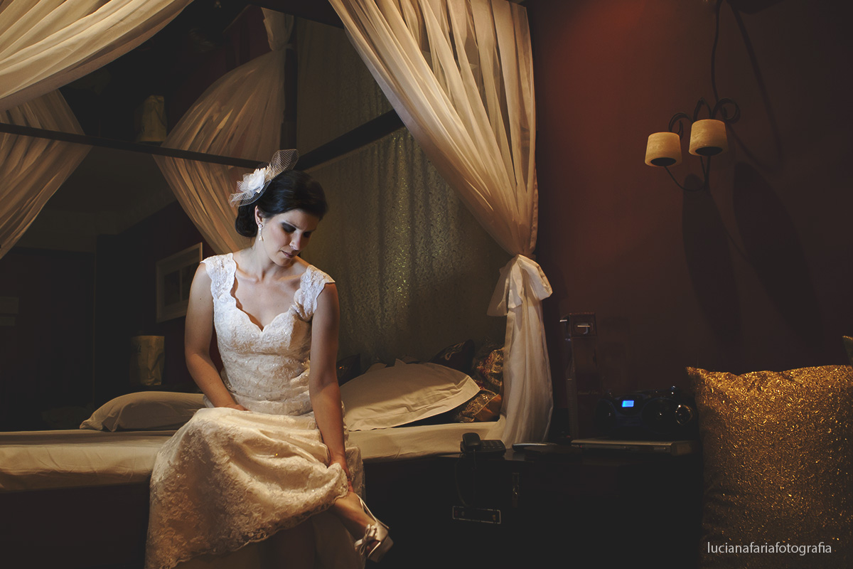 noiva colocando o sapato escolhido para o casamento sapato confortável e elegante sentada na cama com voal no quarto da noiva em lindo registro da fotógrafa de casamento luciana faria de sp