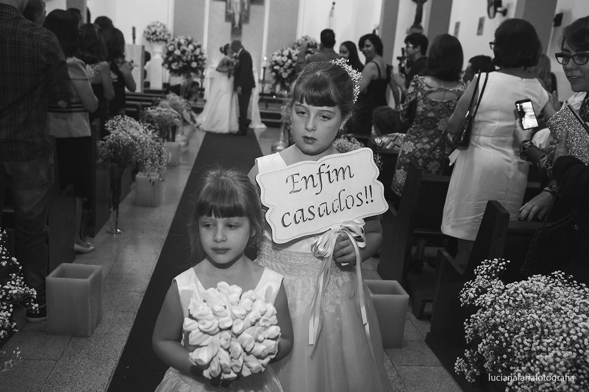 saída dos noivos da igreja com daminha segurando a placa enfim casados fotografia de momento feliz da fotógrafa Luciana Faria em Poços