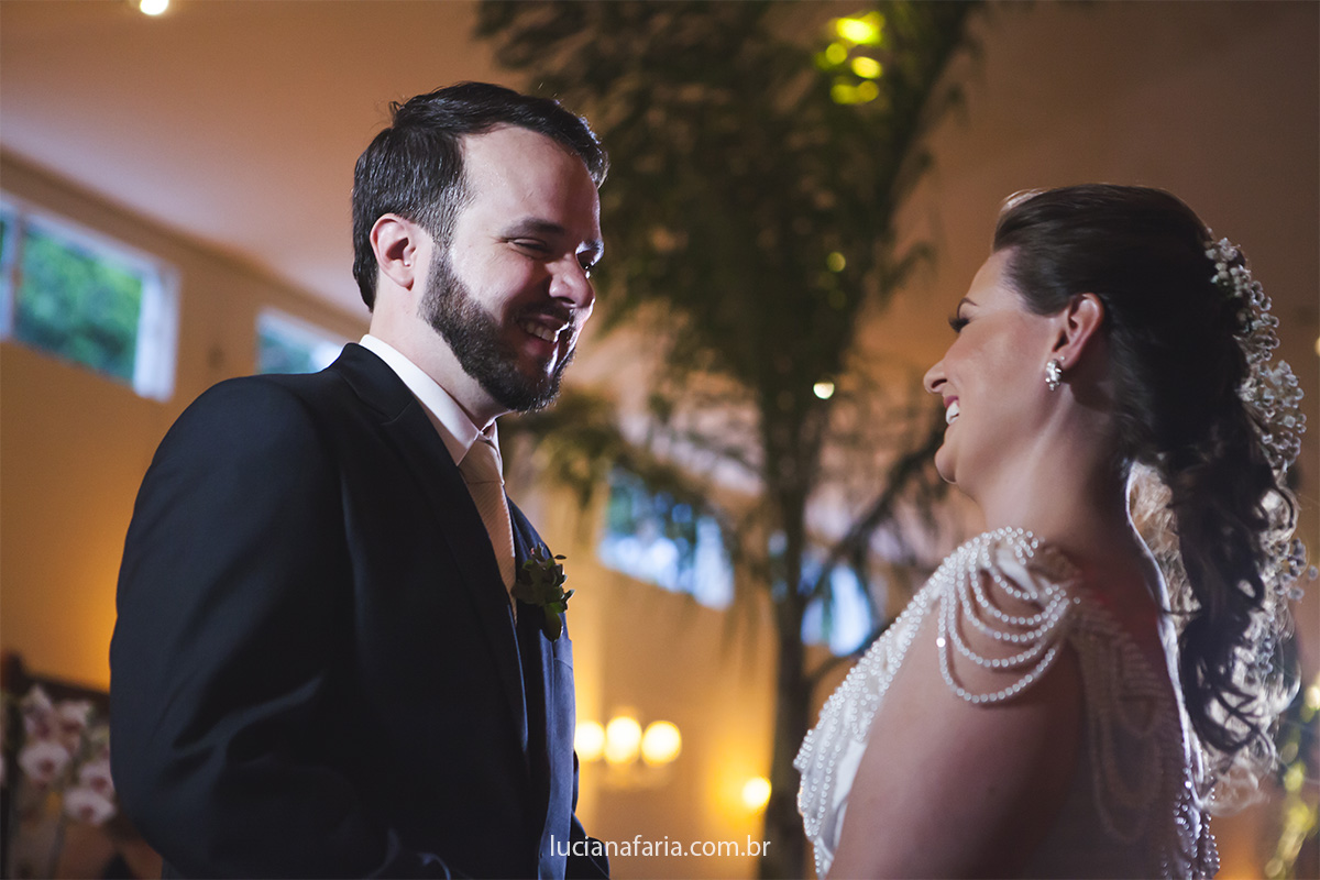 olhares e sorrisos dos noivos nas trocas dos votos num lindo salão decorado pelo papai do céu floricultura de sp registro do casamento com fotografa luciana faria