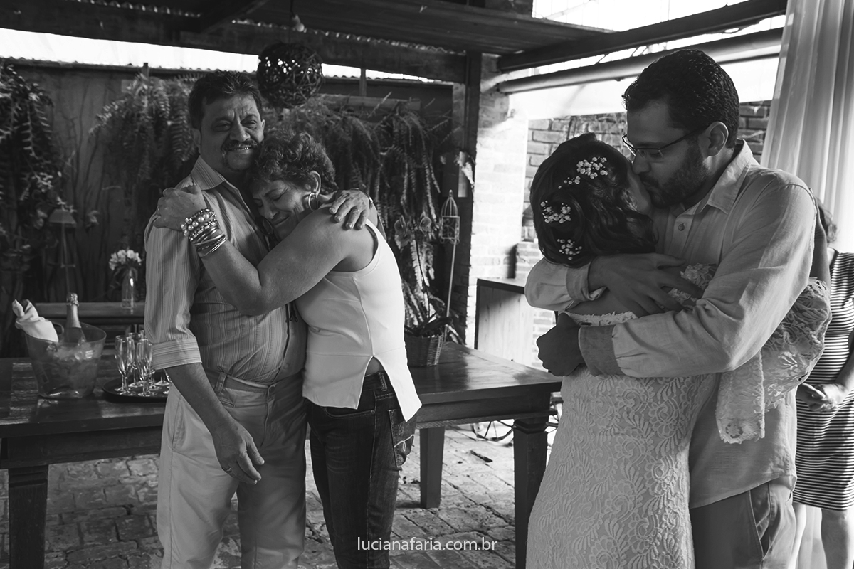 noivos se abraçam e os pais se abraçam no fundo emocionados com o amor do casal
