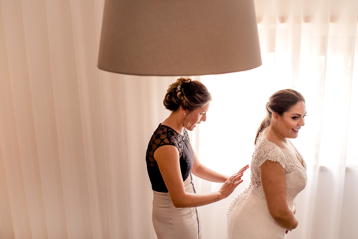 madrinha ajuda noiva a colocar o vestido