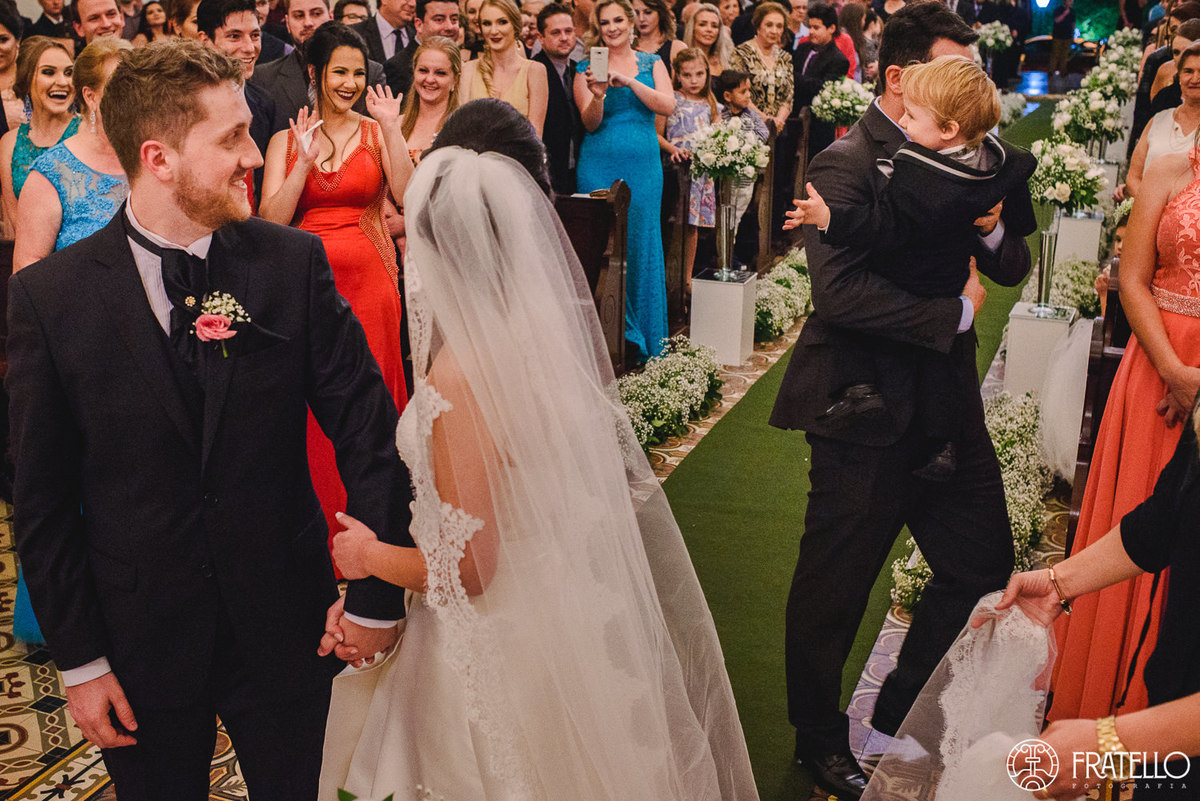 noivinho acenando para os convidados e sendo levado pelo seu pai na igreja matriz nossa senhora da luz em irati