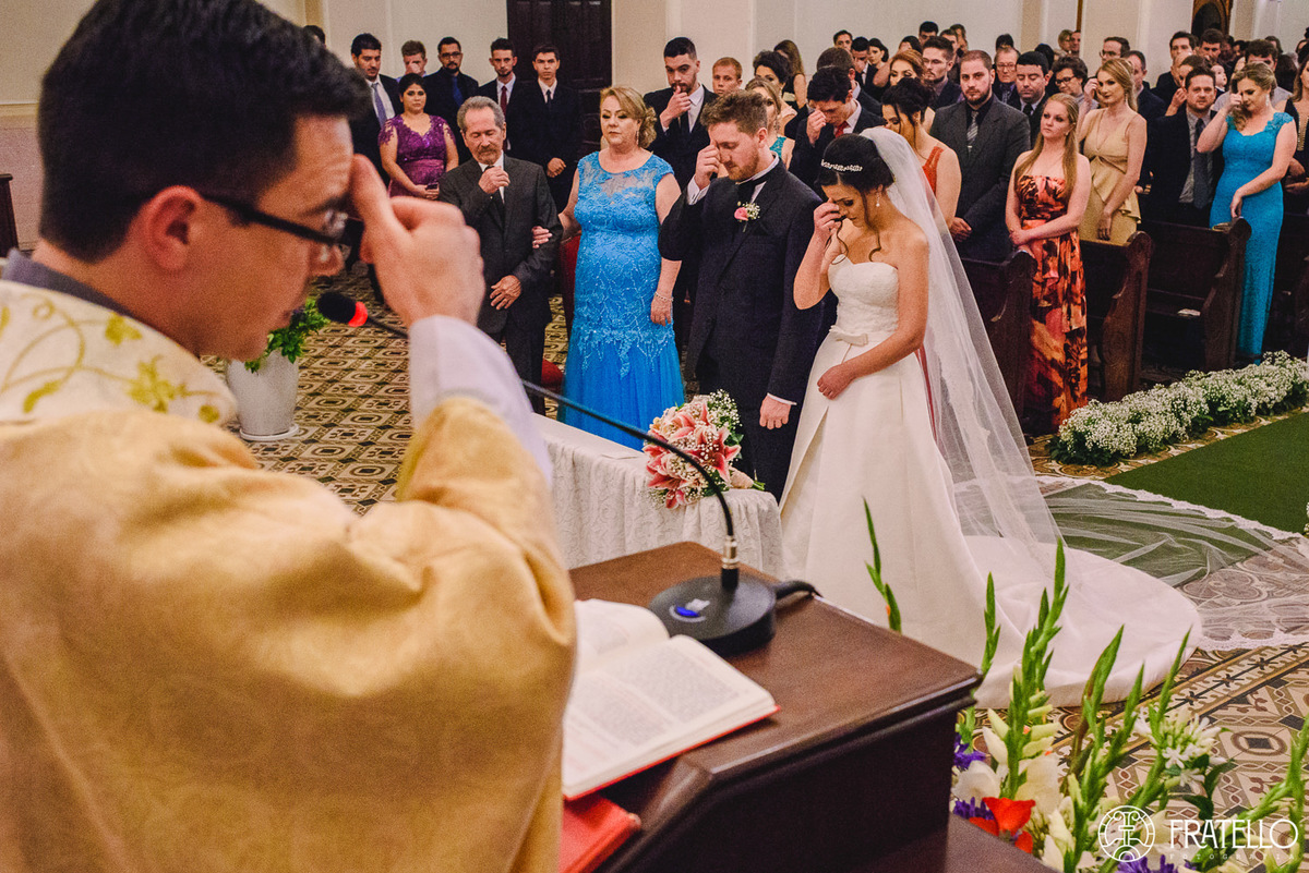 noivos e convidados fazendo sinal da cruz durante o casamento na igreja nossa senhora da luz em irati
