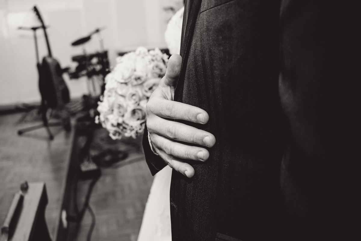 Mão do noivo ao lado de um buquê de rosas branco em um casamento