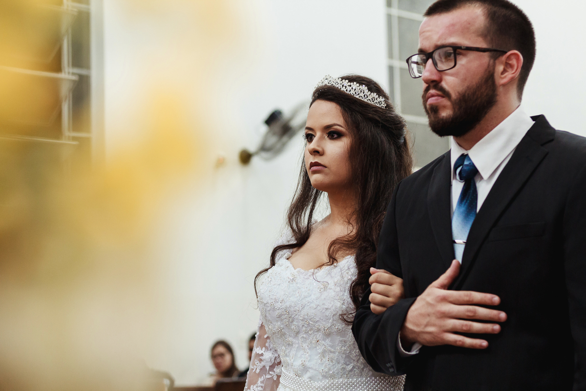 Noivo vestindo um vestido  segurando um buquê de flores cor de rosa ao lado do noivo que veste um lindo terno de casamento