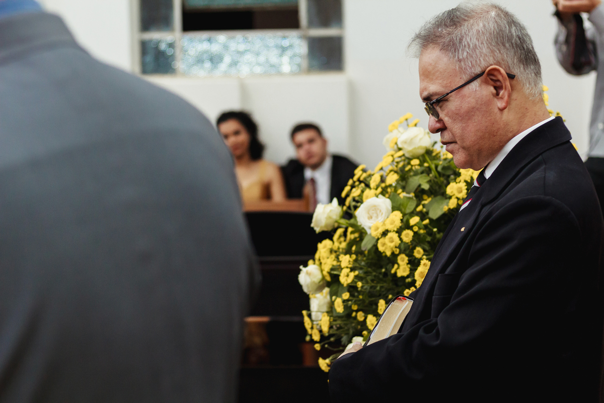 Pastor com a expressão séria em casamento ao lado de flores amarela de decoração