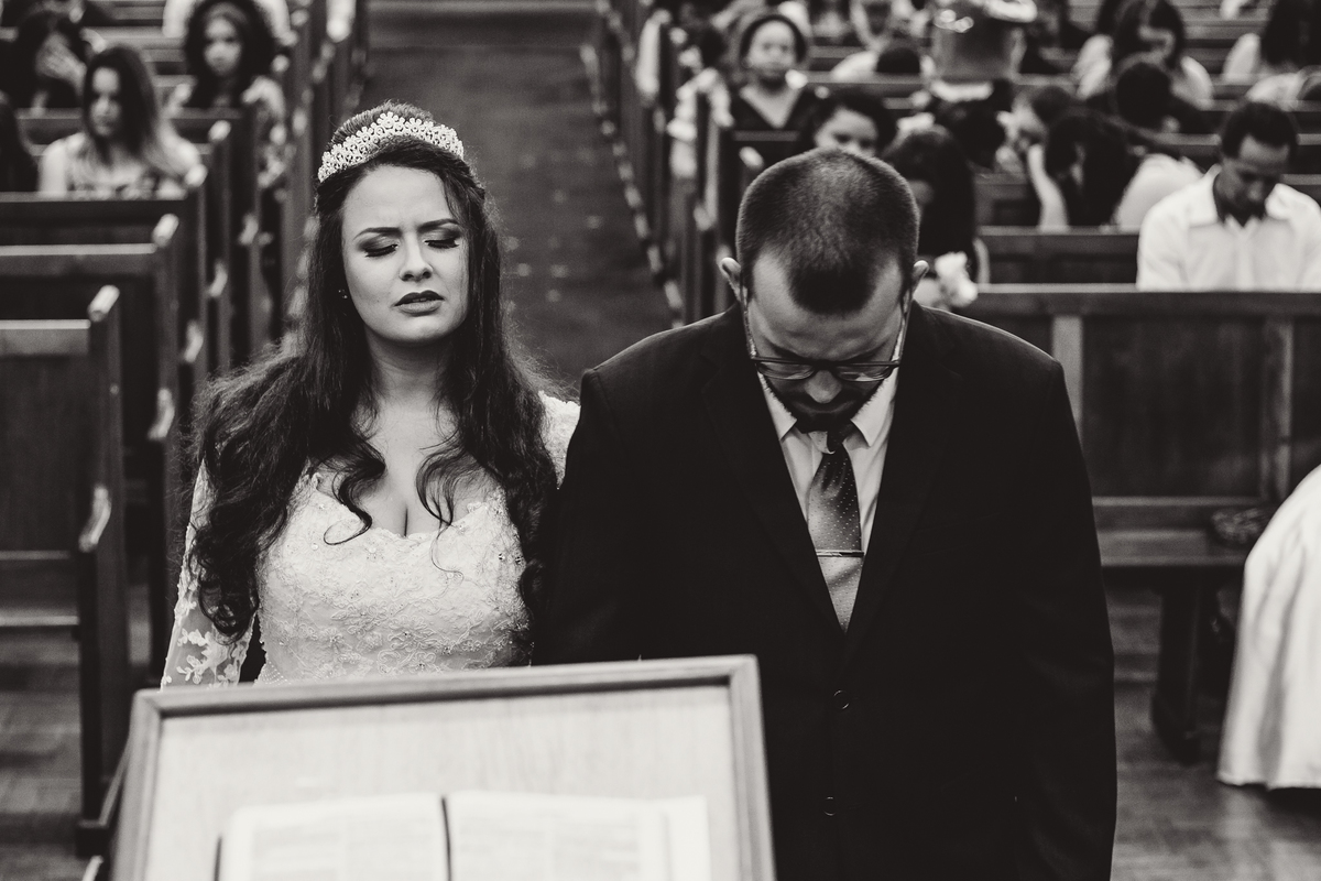 Noiva vestida com vestido branco lindo ao lado do noiva com um terno lindo orando em um momento emocionante durante um casamento