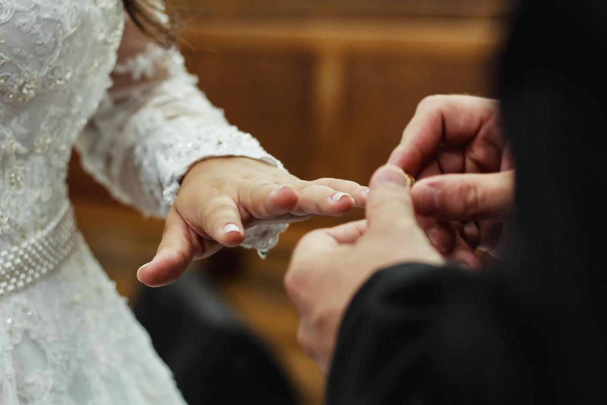 Noivo colocando a aliança na mão da noiva durante a cerimônia de casamento