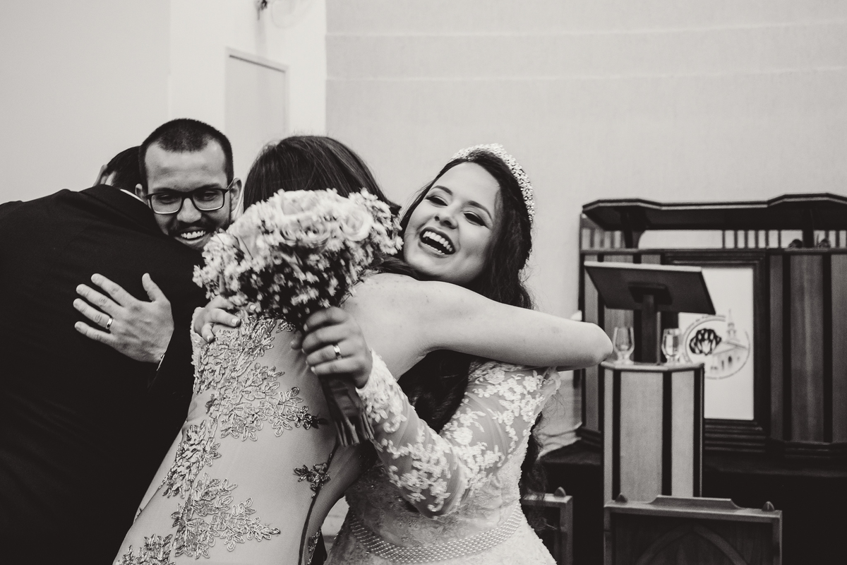 Madrinha cumprimentando a noiva que está sorrindo com o buquê de flores durante o casamento