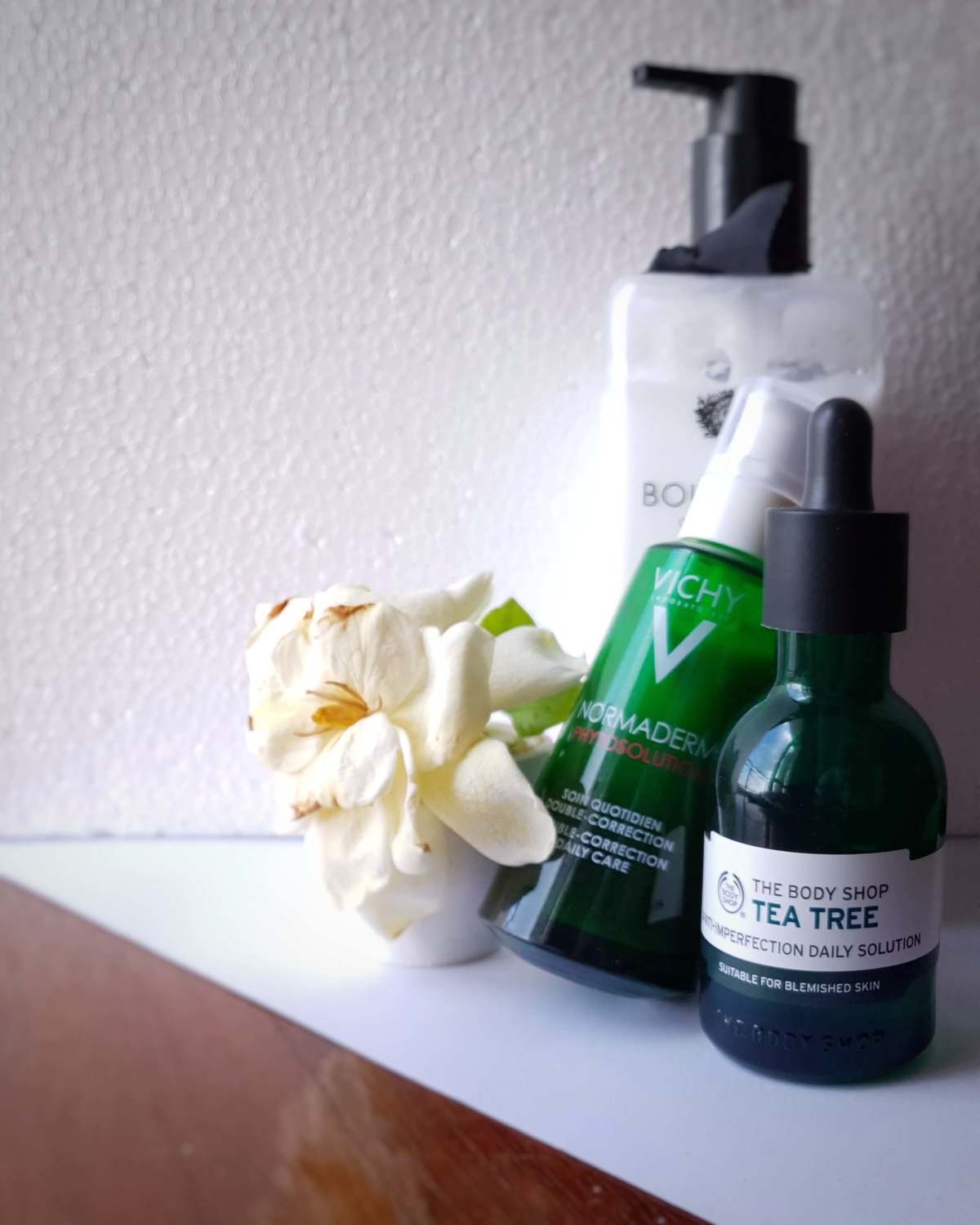 a imagem mostra uma embalagem de hidratante corporal, um vidro de sérum facial com válvula pump, um vidro de sérum facial em conta-gotas e um vaso pequeno com uma flor.