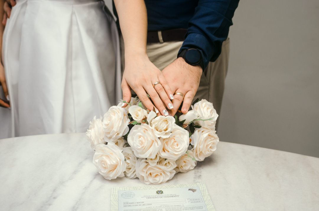 mãos de alianças em cima do buquê