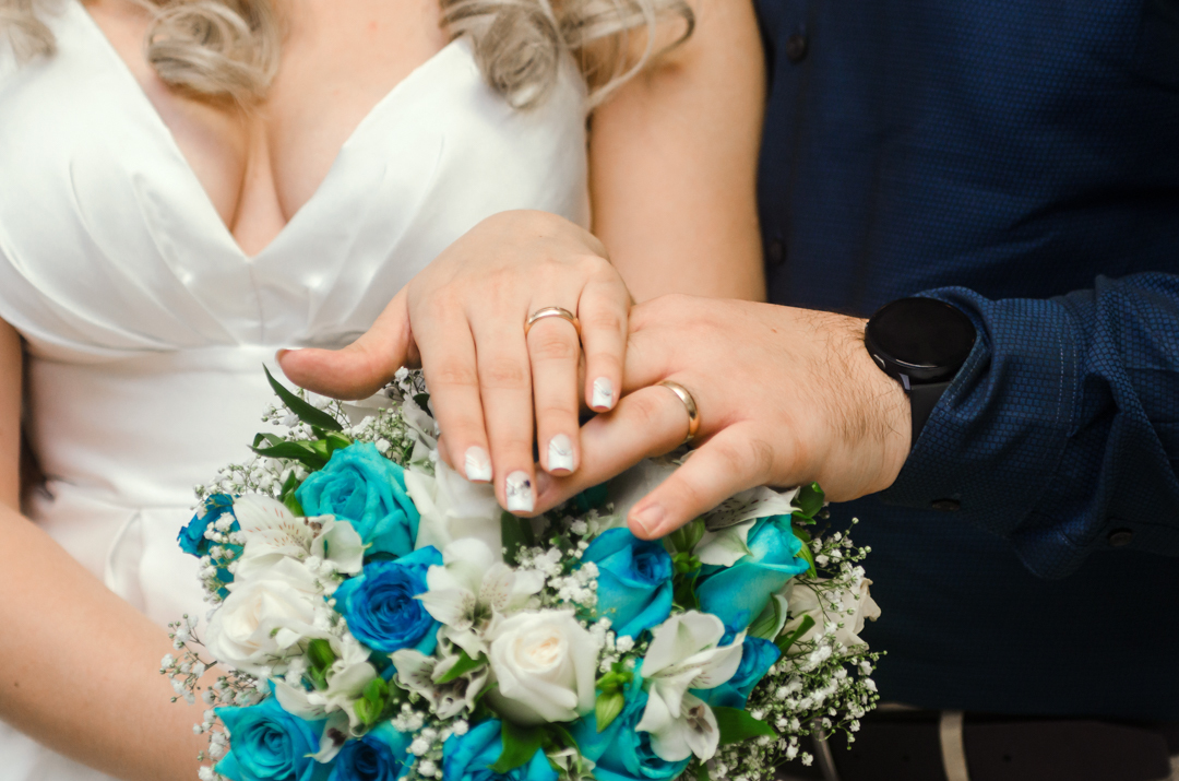 mãos de alianças em cima do buquê