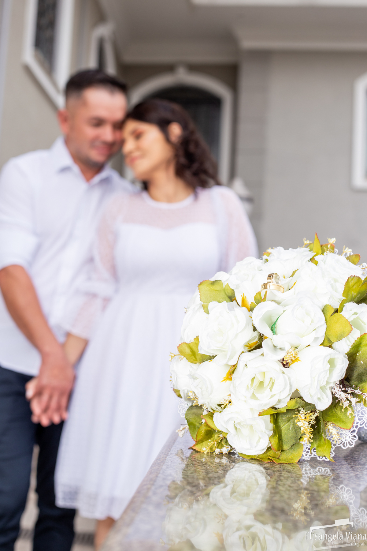 buquê em foco e noivos no fundo