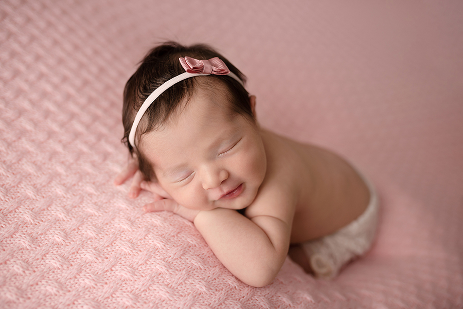 recém nascido sorrindo deitado na manta rosa em ensaio newborn em casa no rio de janeiro