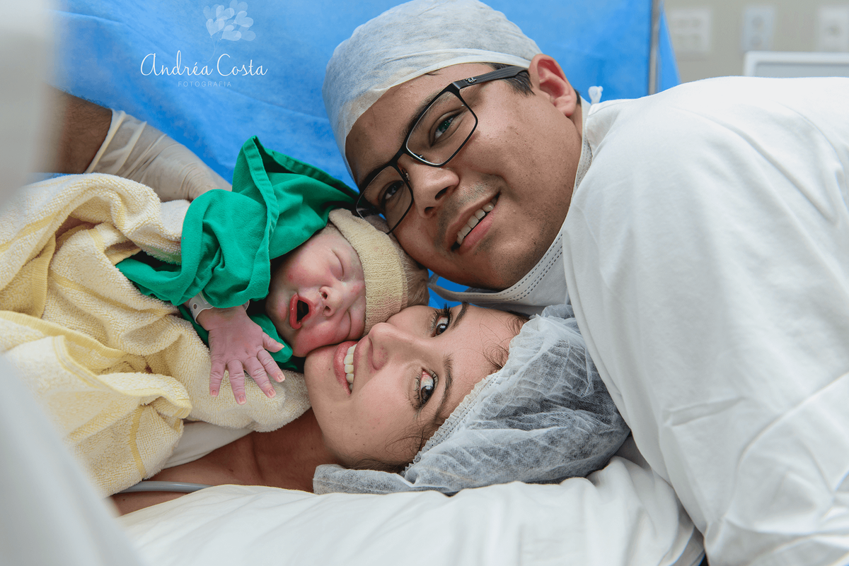 Foto do casal com o bebê recém nascido no centro cirúrgico da perinatal da Barra da Tijuca, por Andréa Costa