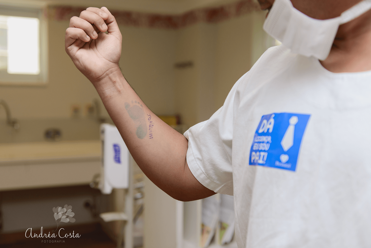 Papai mostrando seu braço com a marca do pezinho do Joaquim, por Andréa Costa