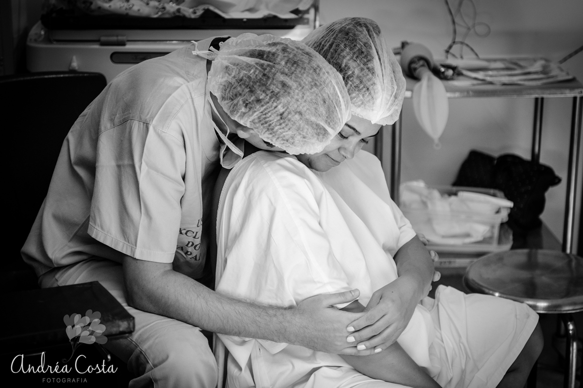 Foto em preto e branco do casal se abraçando na sala de parto, por Andréa Costa