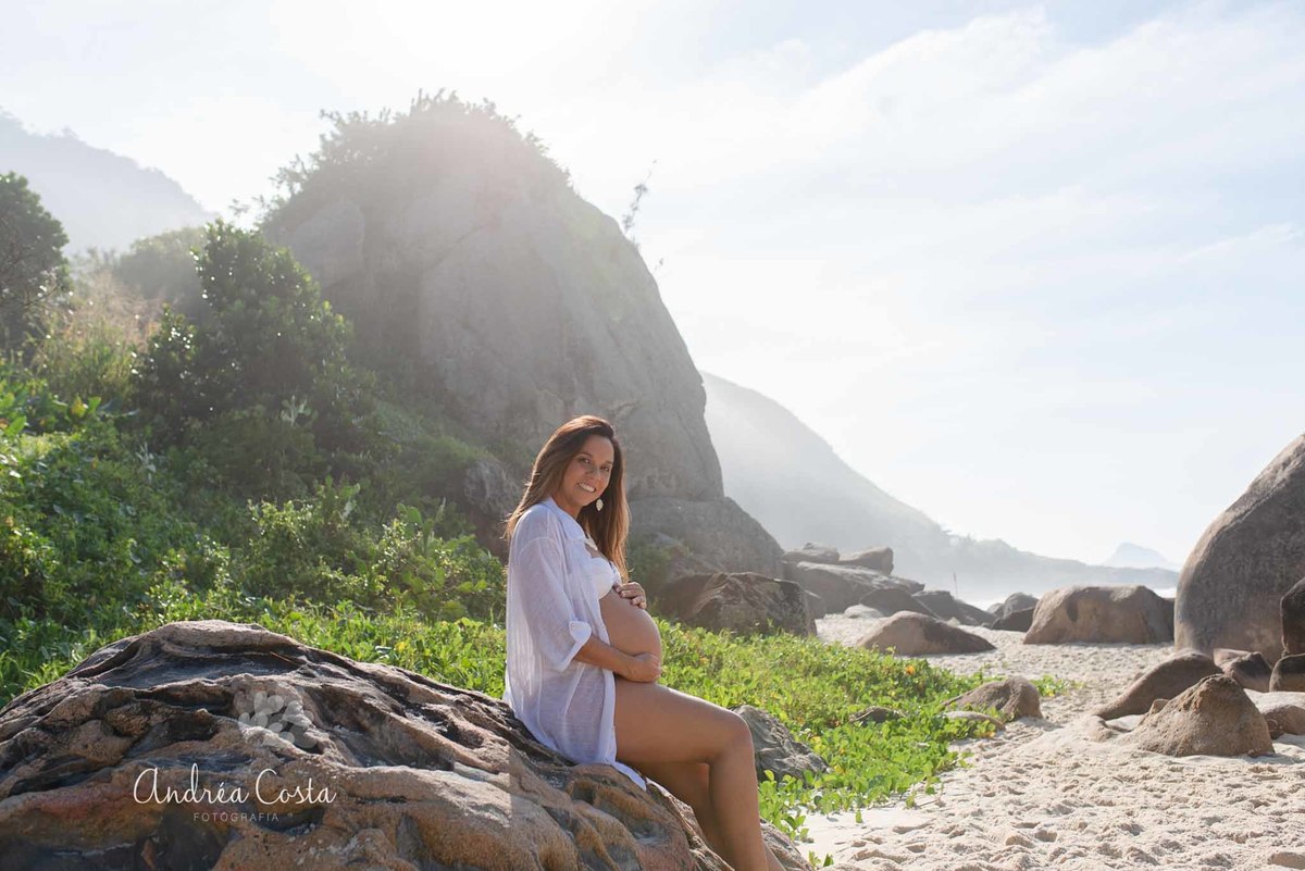 gravida linda sentada na pedra olhando pra câmera em book gestante