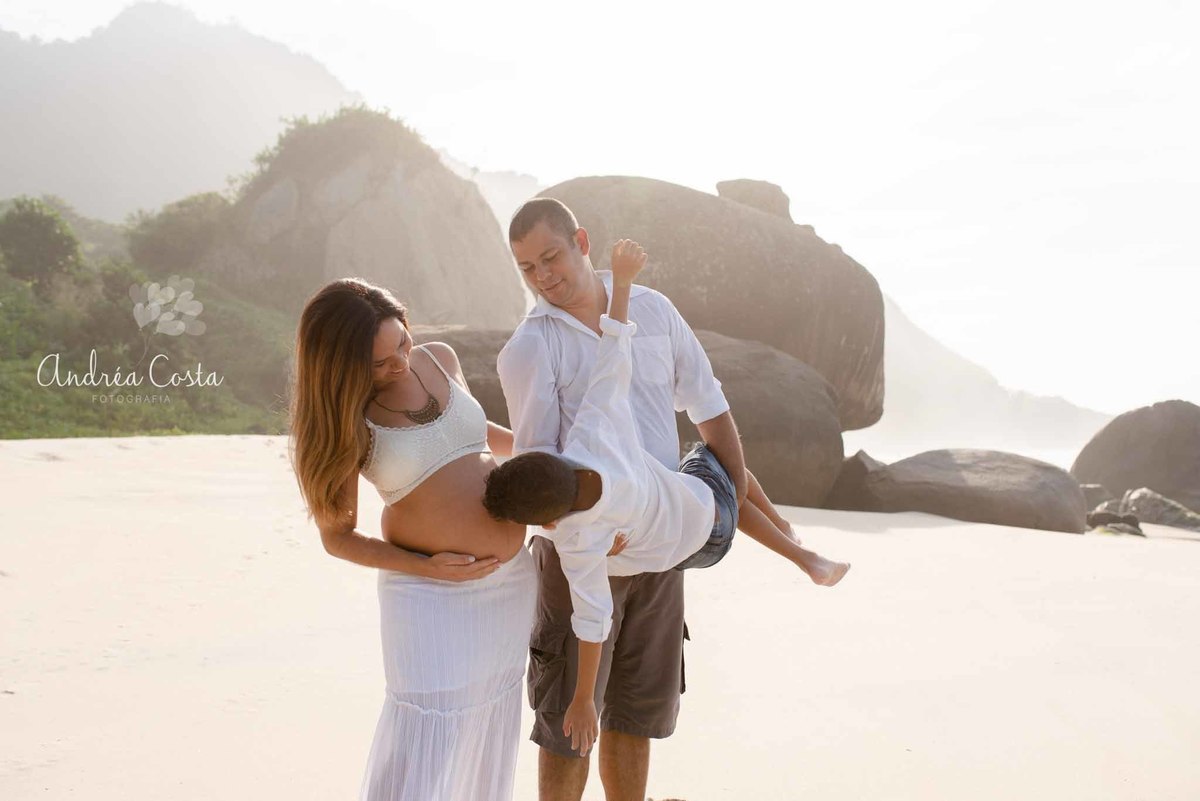 filho mais velho beijando a barriga da mamae em lindo ensaio gestante na praia da barra da tijuca no rio de janeiro