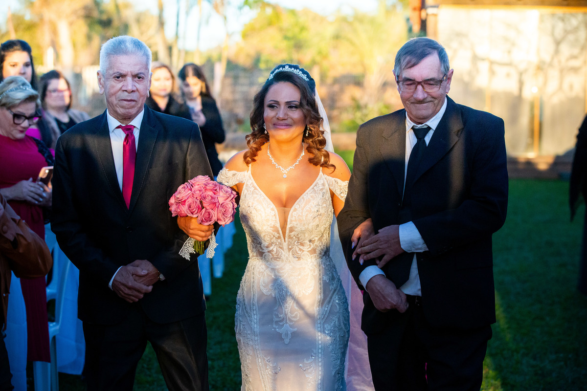 Noiva caminhando para a cerimônia acompanhada de familiares, em um momento emocionante do casamento.