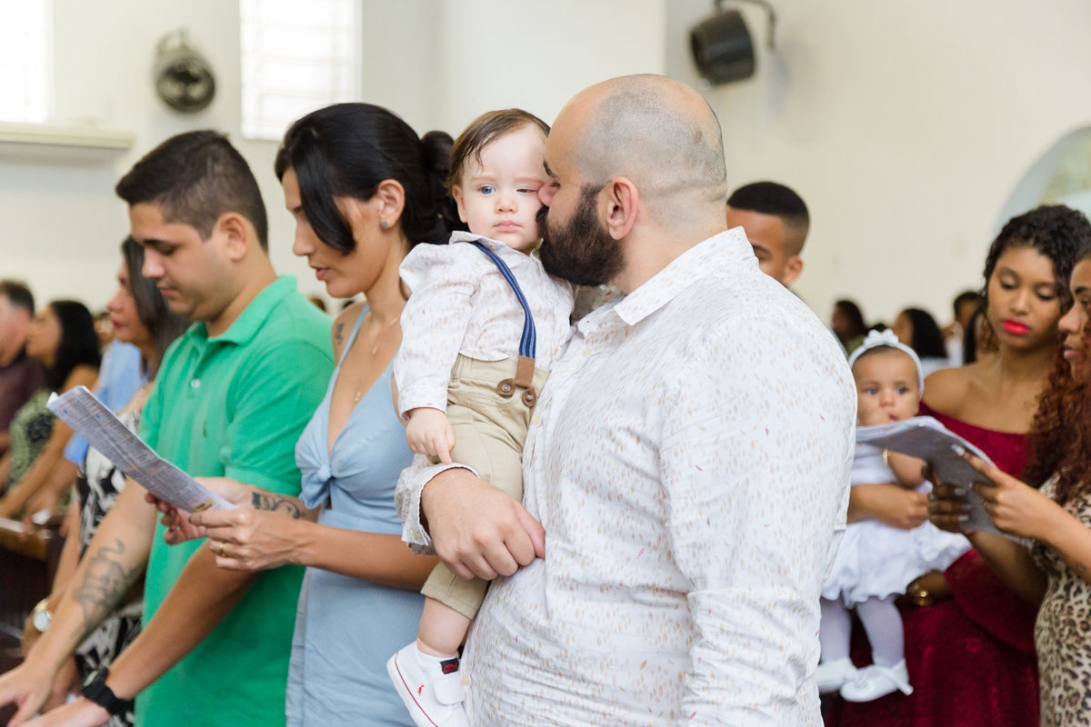 Pai beijando criança durante cerimônia de batismo enquanto mãe e padrinho rezão