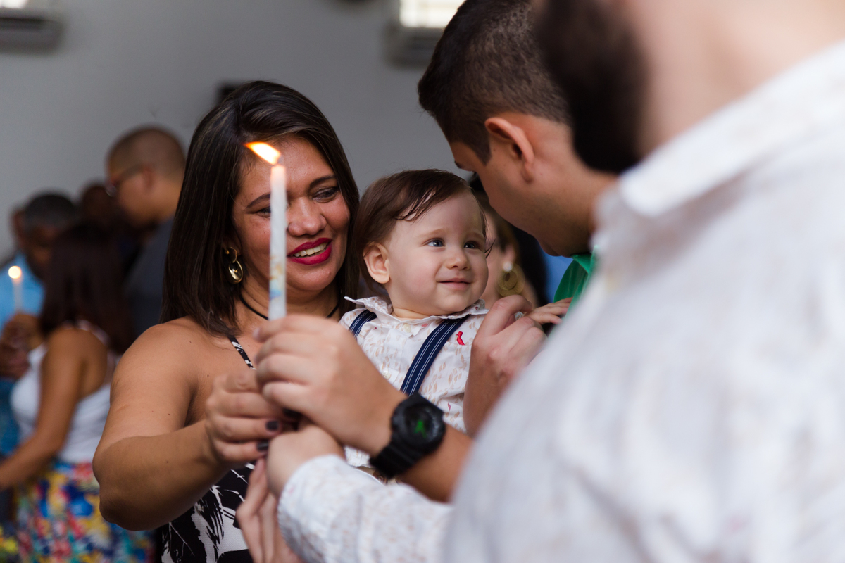Padrinhos seguram a vela do batizado e a criança olha para o padrinho