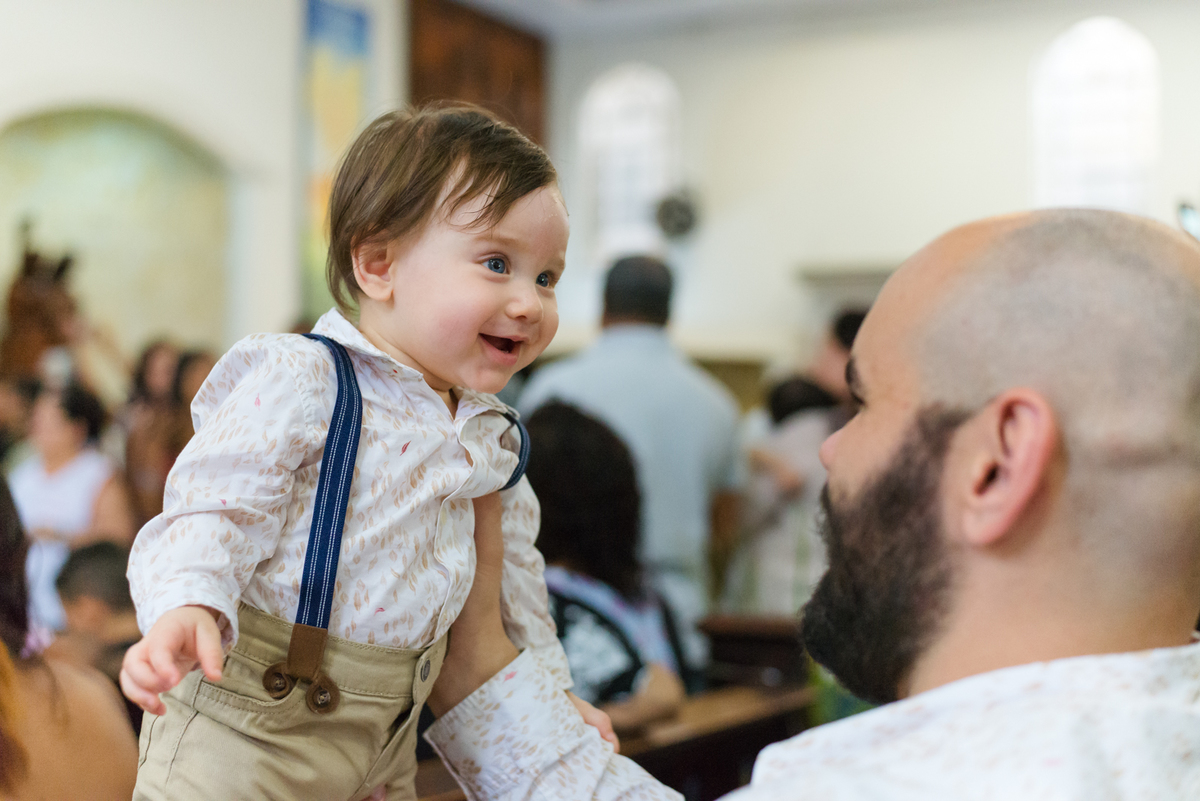 Pai erque filho e o filho sorri durante a cerimônia de batismo