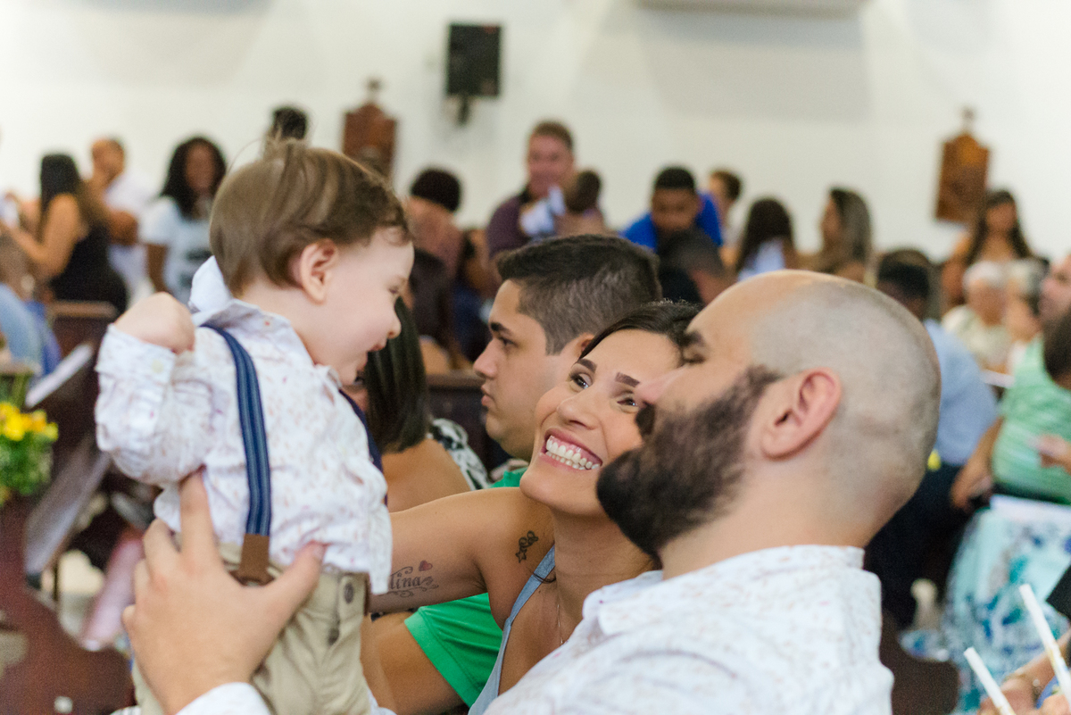 Pais erquem filho e sorriem para ele  durante cerimônia de batismo