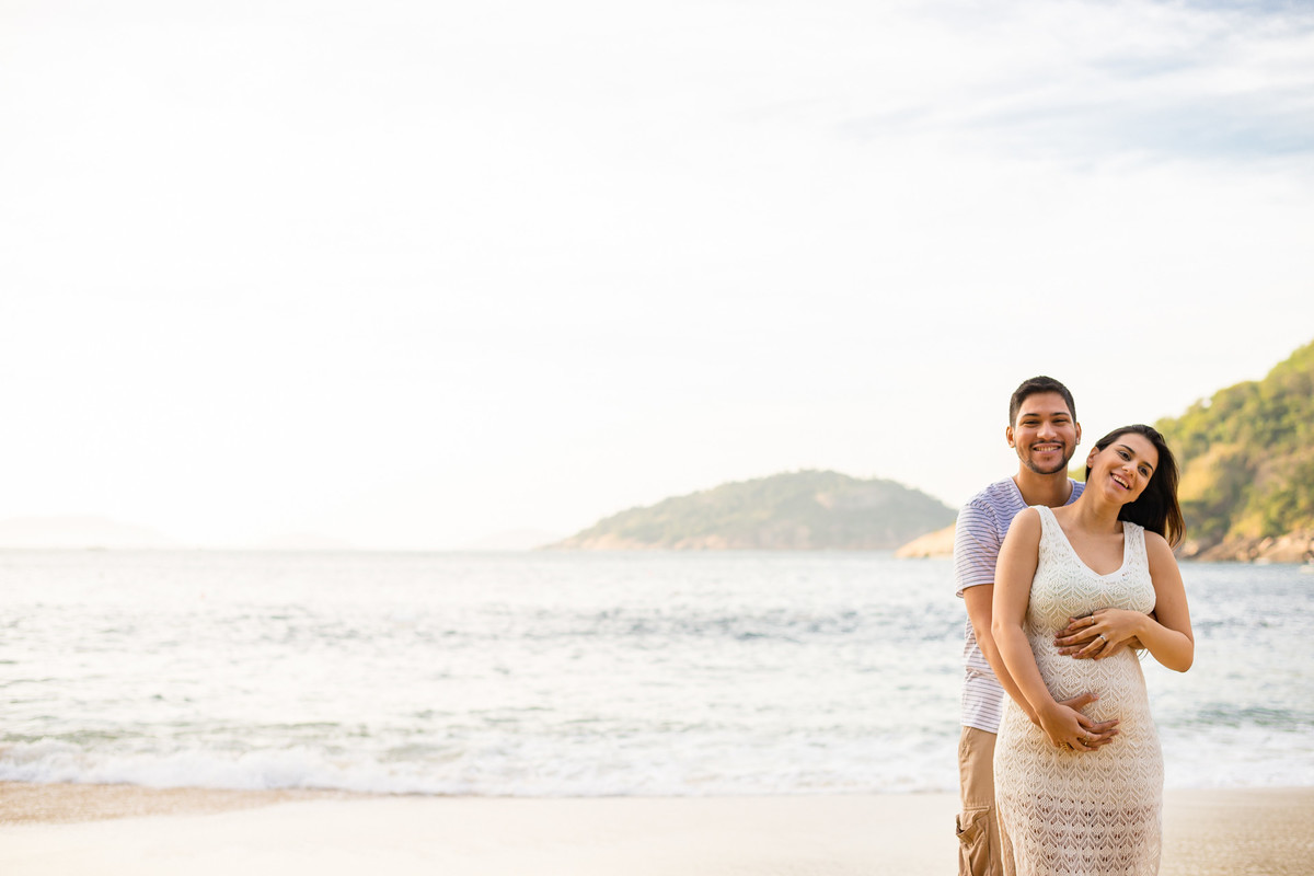 mamãe e papai sorrindo e abraçando a barriga na praia vermelha