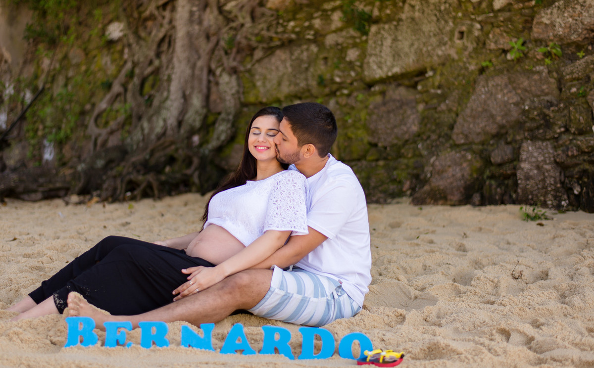 papais se beijando sentados na areia da praia vermelha com as letras formando o nome do bebê