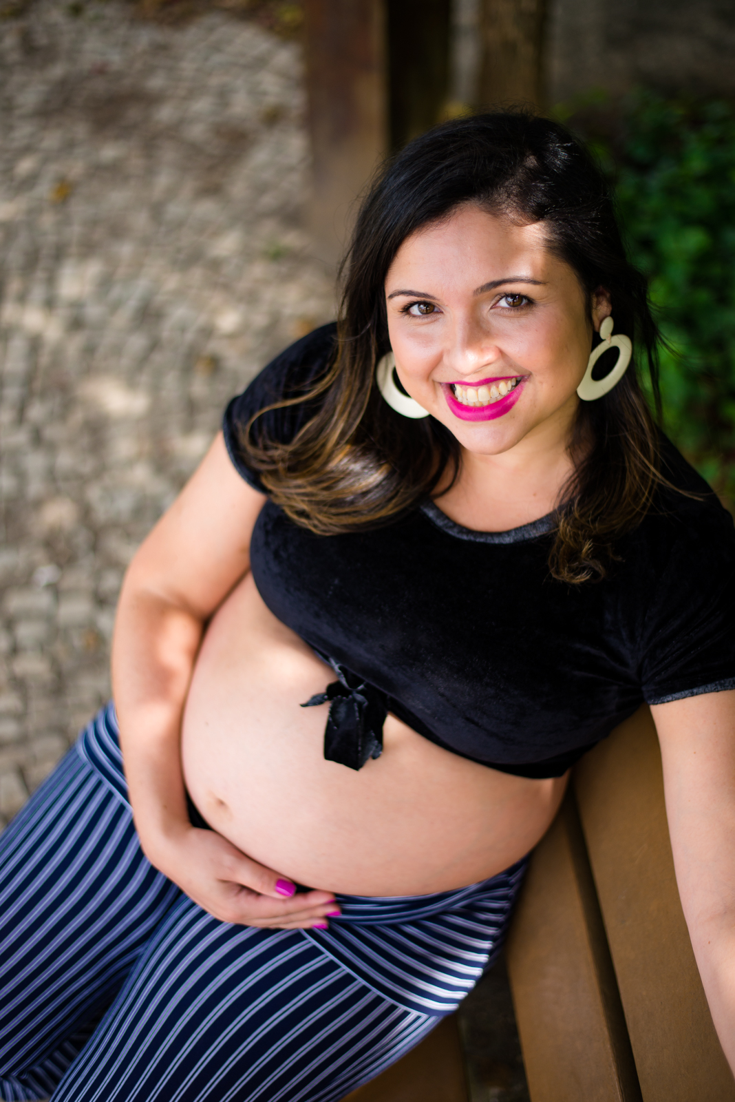 Mamãe feliz com as mãos no seu barrigão registrado pelo fotógrafo de gestante Nós Dois Fotografia na Barra da Tijuca RJ num belo jardim de fundo